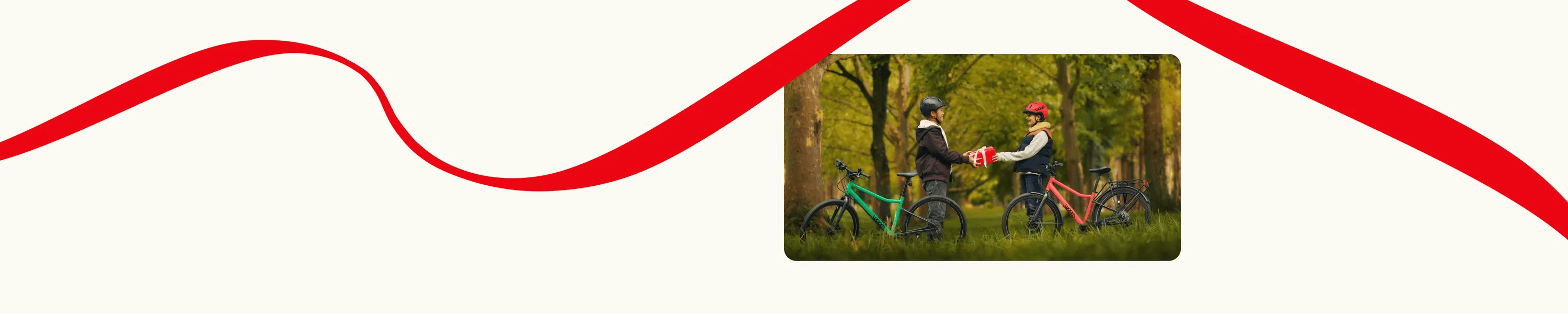 Two kids with woom EXPLORE bikes in a forest are exchanging a gift. Decorative red lines frame the scene.