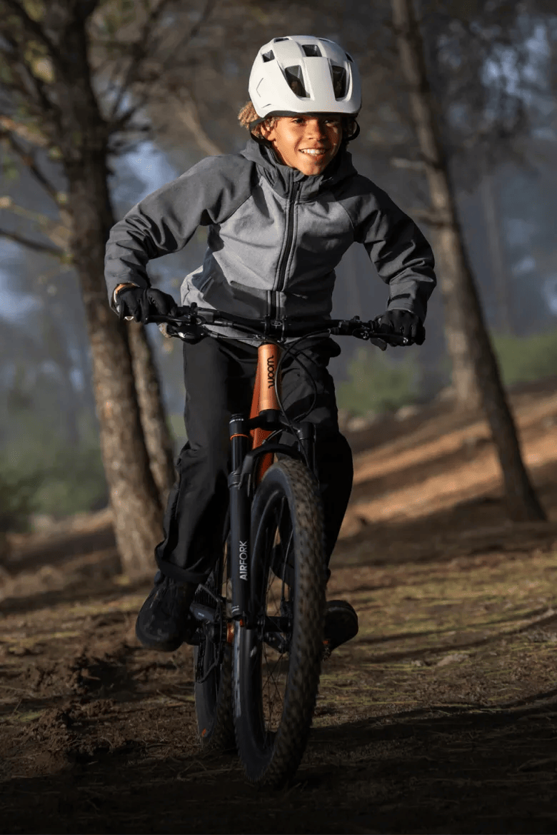 Kind mit weißem woom READY Kinderhelm auf einem woom OFF Mountainbike im Wald.