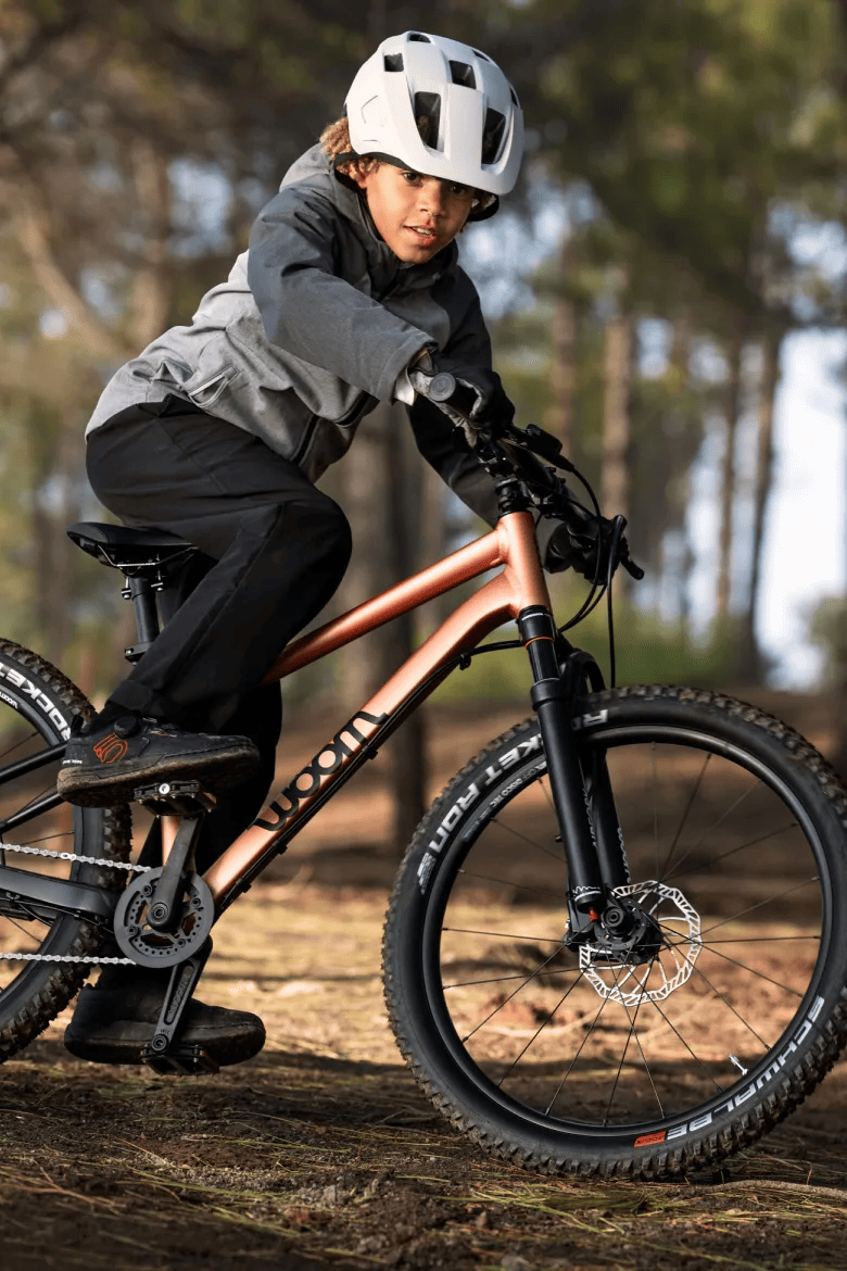 A boy sitting on his woom OFF mountain bike on a sunny forest path.