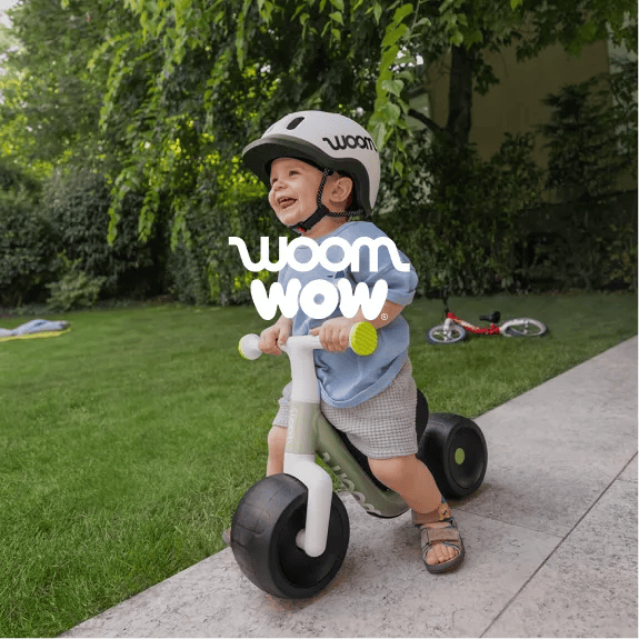 An image of a very young boy in a yard wearing a READY Helmet while riding a woom WOW in soft sprout.