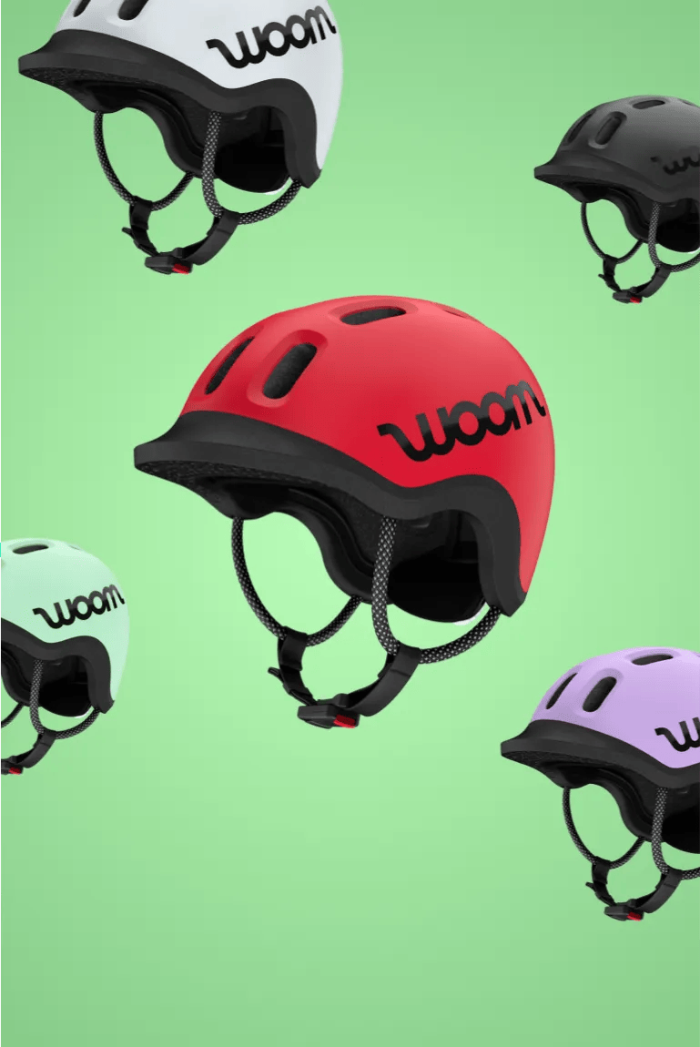 READY Fahrradhelme von woom in den 5 Farben woom red, mint, lilac, pale grey und charcoal metallic vor grünem Hintergrund