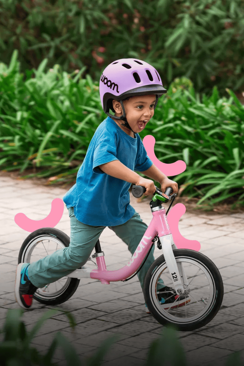 Kind mit lila woom READY Kinderhelm auf einem pinken woom GO 1 Laufrad.