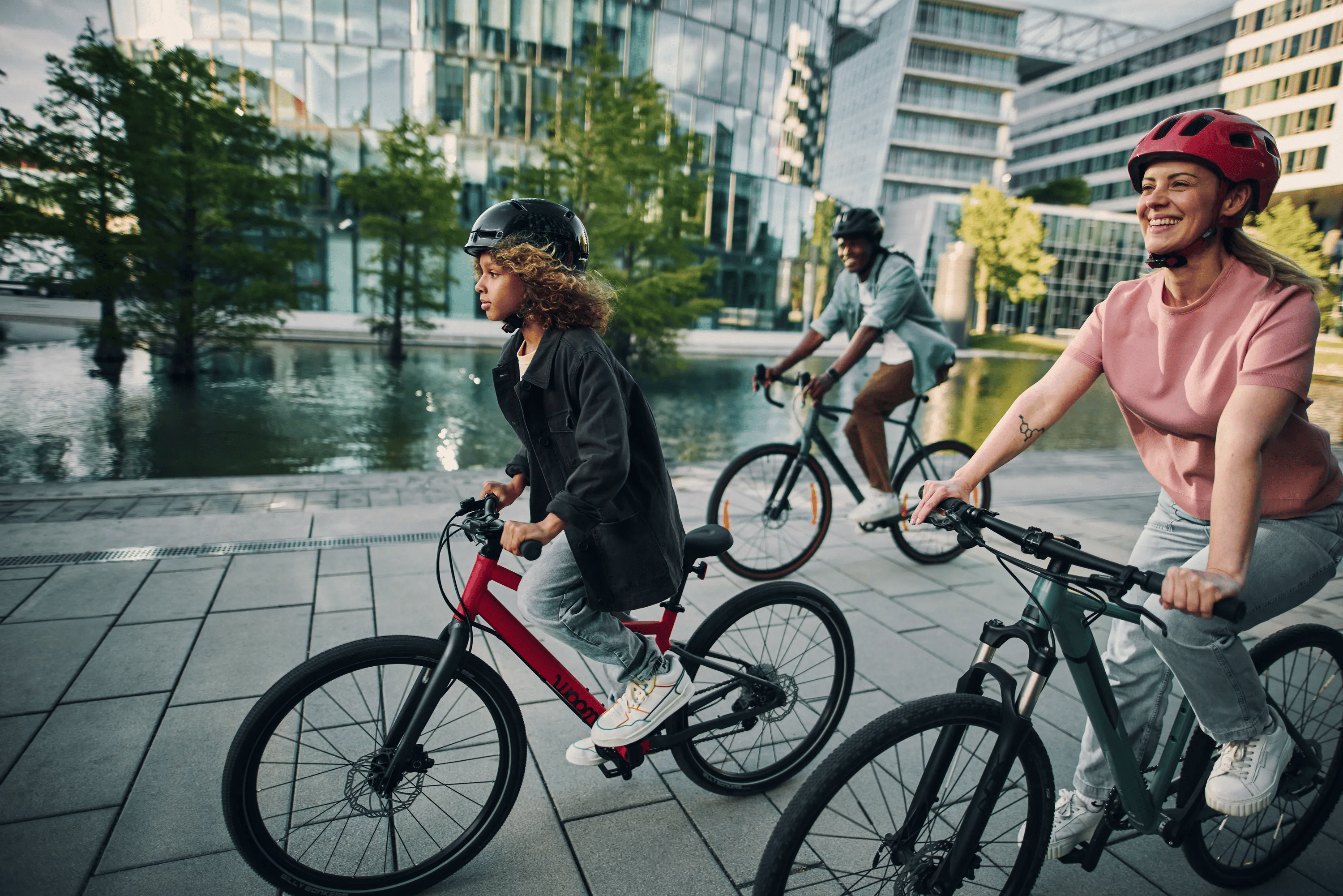 Un garçon traverse la ville sur un vélo rouge woom EXPLORE 5 de 24 pouces, accompagné de sa mère et de son père.