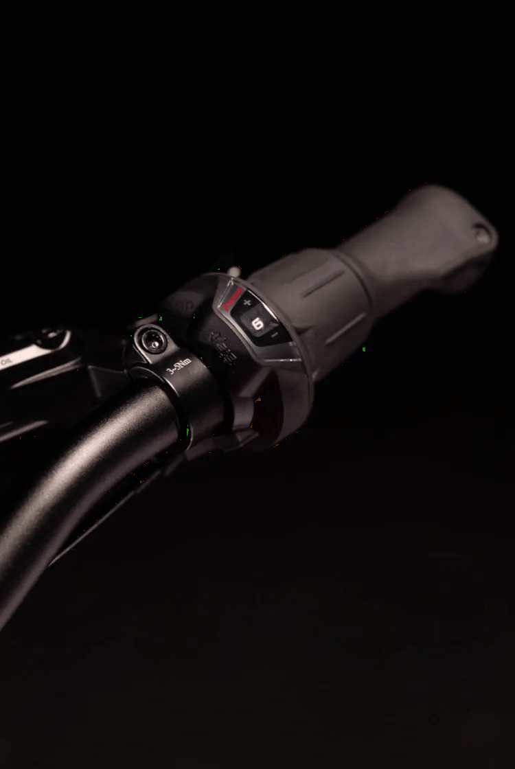 Zbliżenie na czarną kierownicę woom EXPLORE oraz czarną manetkę obrotową Shimano z wskaźnikiem biegu.