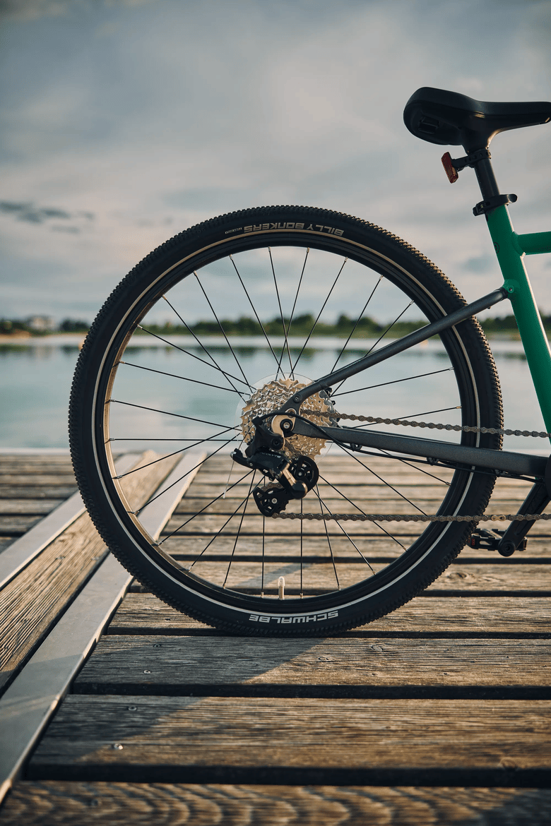 A wheel of a green woom EXPLORE bike standing on a wooden pier.